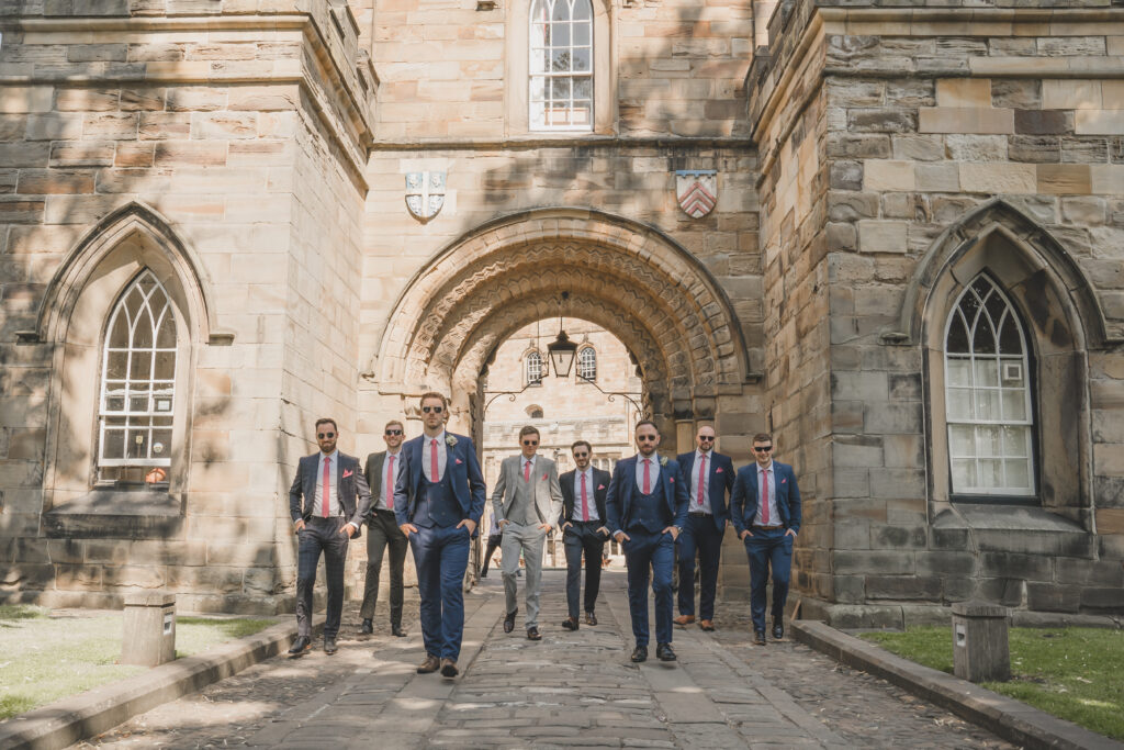 A group of groomsmen standing in front of a stone building.