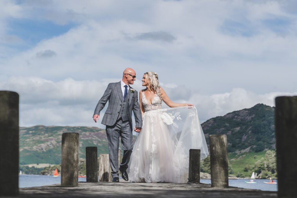 A bride and groom standing on a dock in the lake district.